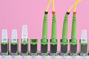 Das Bild zeigt 4 grüne Glasfasern, die in einen Glasfaserstecker eingesteckt sind.