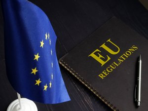 zu sehen ist ein Schwarzes Buch mit dem Titel "EU Regulations", daneben die blaue EU Flagge mit gelben Sternen