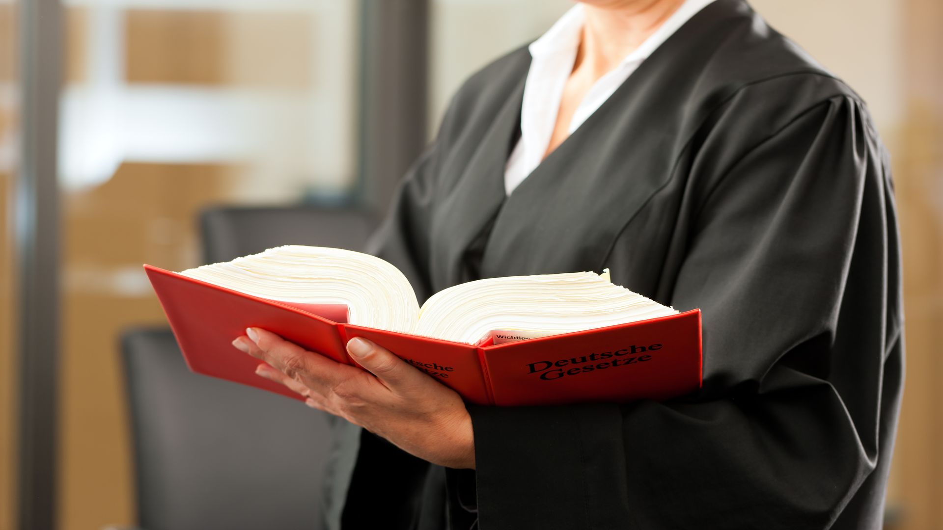 Foto eine*r Richter*in in Robe mit rotem Gesetzesbuch in der Hand