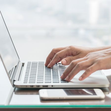 Foto am Laptop arbeitende Person mit Handy